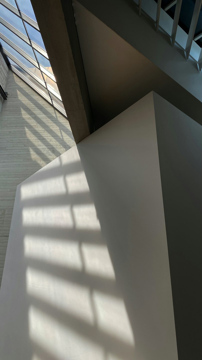 La luce del sole proietta ombre geometriche su un muro di cemento grigio.